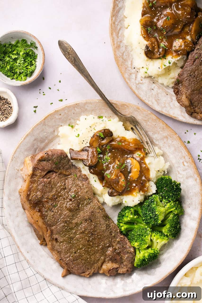 Juicy New York strip steak topped with homemade beef gravy on a plate with mashed potatoes and broccoli.
