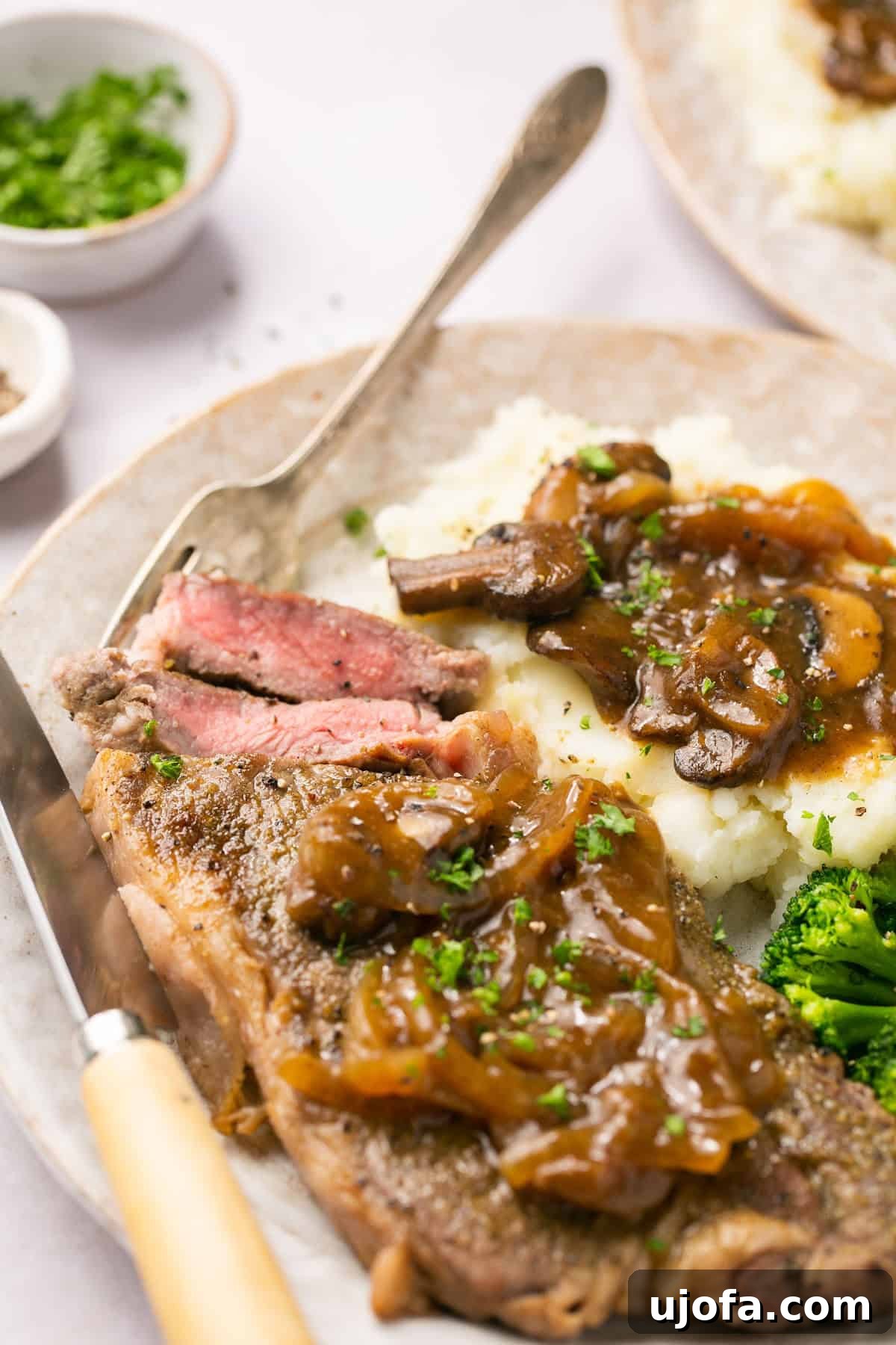 Close-up of cut Instant Pot steak with rich onion-mushroom gravy, served with mashed potatoes and broccoli.