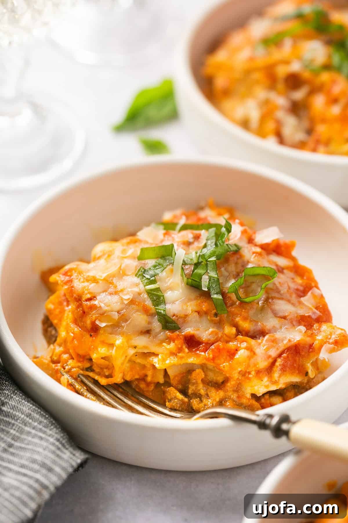 A close-up shot of a perfectly layered slice of Instant Pot lasagna with gluten-free noodles, served in a white bowl with a fork resting on the side, showing the rich texture and melted cheese.