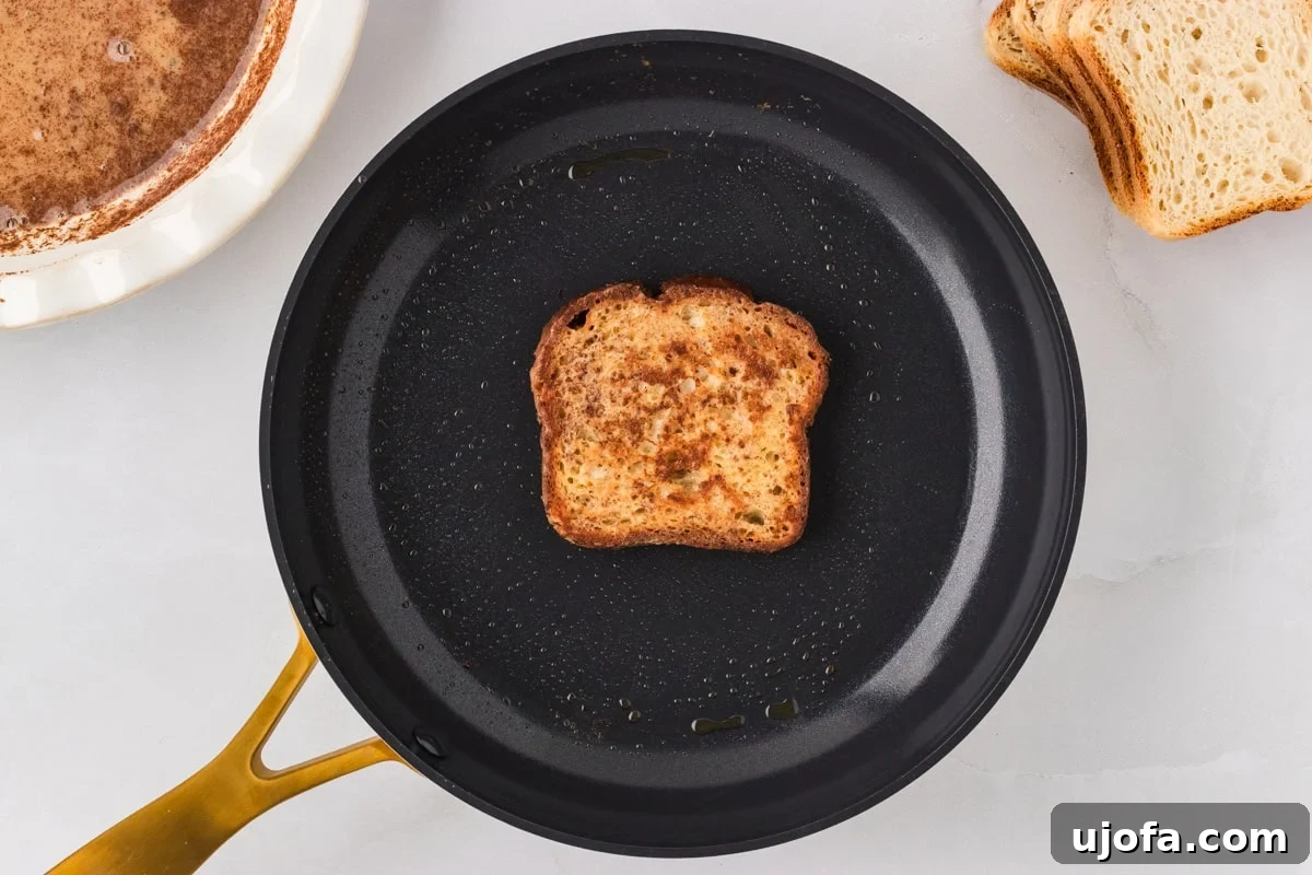 A single slice of gluten-free French toast cooking in a nonstick skillet, starting to brown on one side.