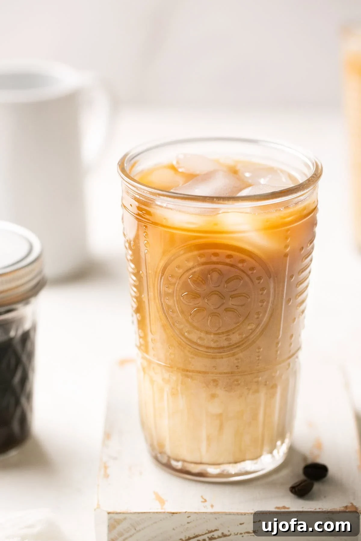 A closeup of a glass of shaken espresso with oatmilk over ice, elegantly placed next to a jar of brown sugar syrup, highlighting the delicious homemade result.