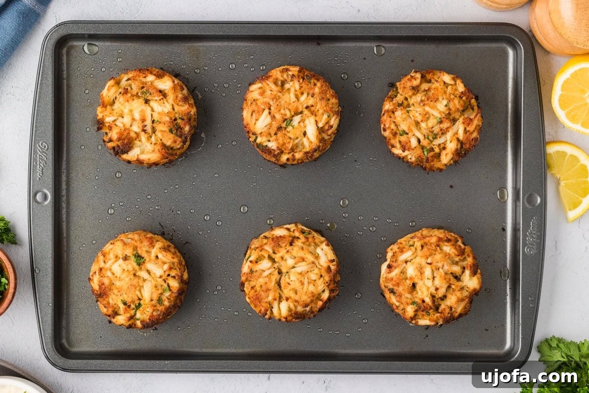 Baked gluten-free crab cakes fresh out of the oven, golden and crisp, resting on a baking sheet with a slight sheen from butter.