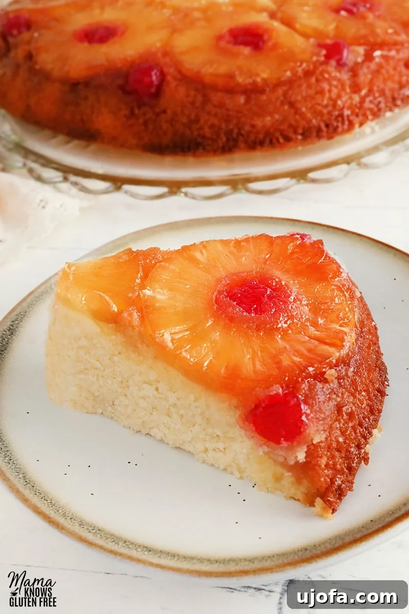 Delicious Gluten-Free Pineapple Upside Down Cake Dairy-Free Friendly 4 A perfectly sliced piece of gluten-free pineapple upside down cake on a white plate, with the remainder of the cake in the background, showing its beautiful topping and moist texture.