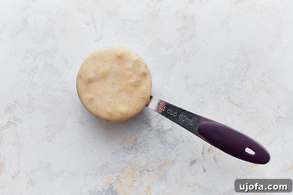 A measuring cup filled to the brim with thick, creamy gluten-free banana pancake batter, demonstrating its readiness for cooking.