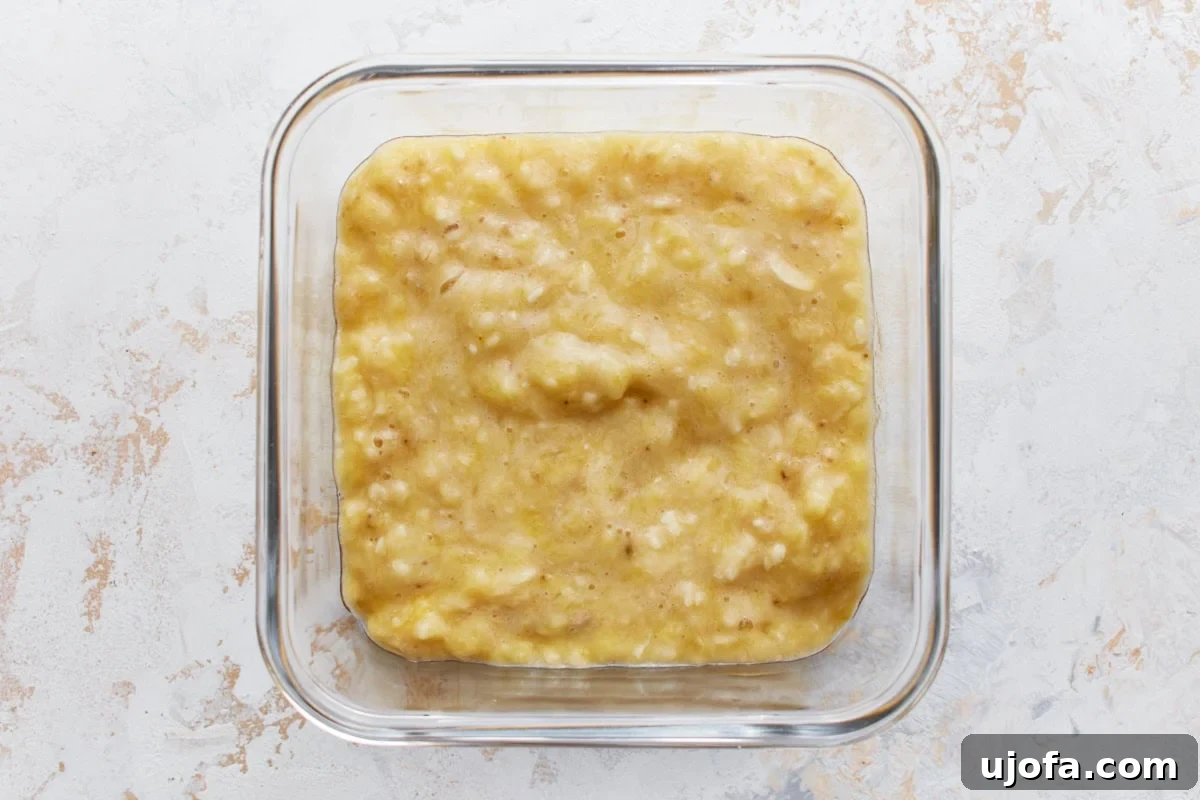A close-up of beautifully mashed ripe bananas in a clear glass container, their creamy texture perfectly prepared for incorporation into the gluten-free banana pancake batter.