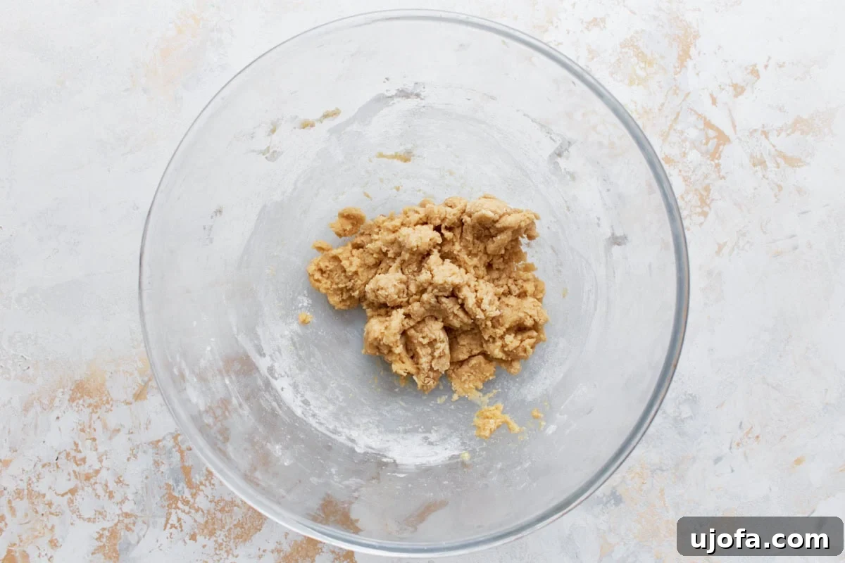 A crumbly, slightly textured dough-like mixture of the initial dry and wet ingredients for gluten-free banana pancakes, resting in a clear glass mixing bowl, signaling readiness for the next liquid addition.