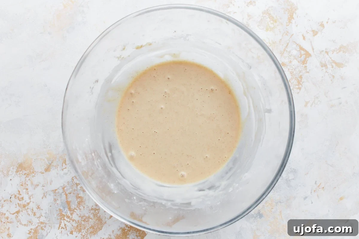 A smooth, golden pancake batter for gluten-free banana pancakes, perfectly mixed and displayed in a clear glass mixing bowl, showcasing its readiness for the final banana addition.