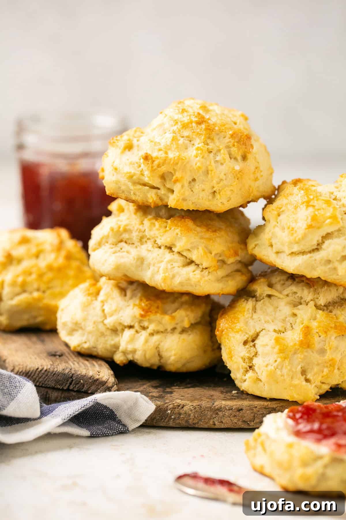 A stack of golden-brown fluffy gluten-free biscuits on a wooden cutting board, with a jar of fruit jam in the soft-focus background, highlighting their rustic charm and delicious appeal.