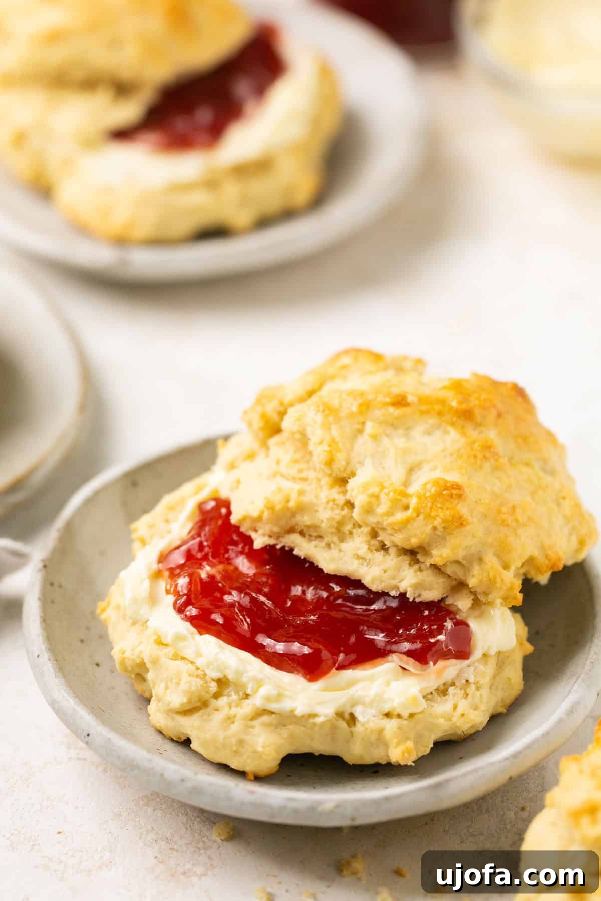 A gluten-free biscuit cut in half, revealing its fluffy interior, served on a gray plate with a dollop of butter and a spoonful of jam, ready to be enjoyed.