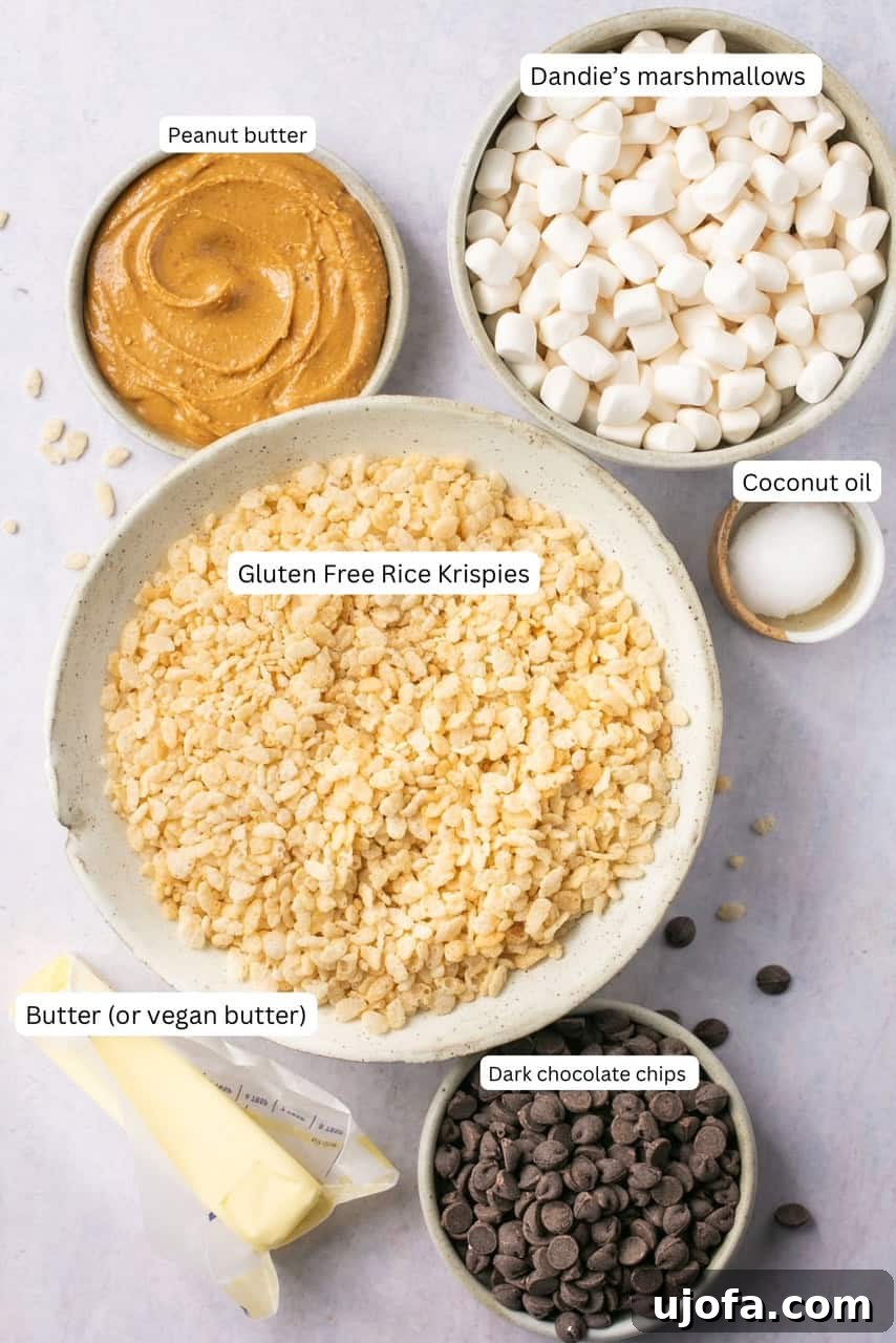 Labeled bowls containing gluten-free rice krispies, vegan marshmallows, vegan butter, creamy peanut butter, dark chocolate chips, and coconut oil, set against a light background.