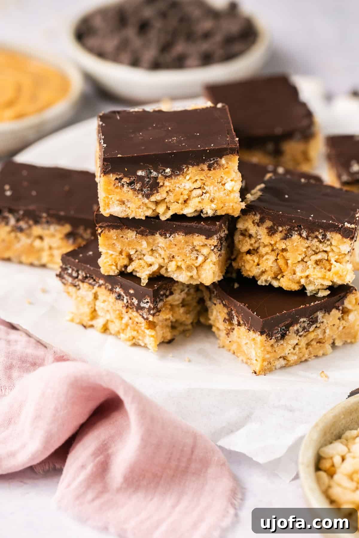 A tall stack of chocolate-covered rice krispie treats layered on parchment paper, highlighting their delicious texture and inviting appearance.