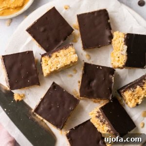chocolate peanut butter rice krispie treats laid out on parchment paper with a bowl of peanut butter and marshamllows in the background