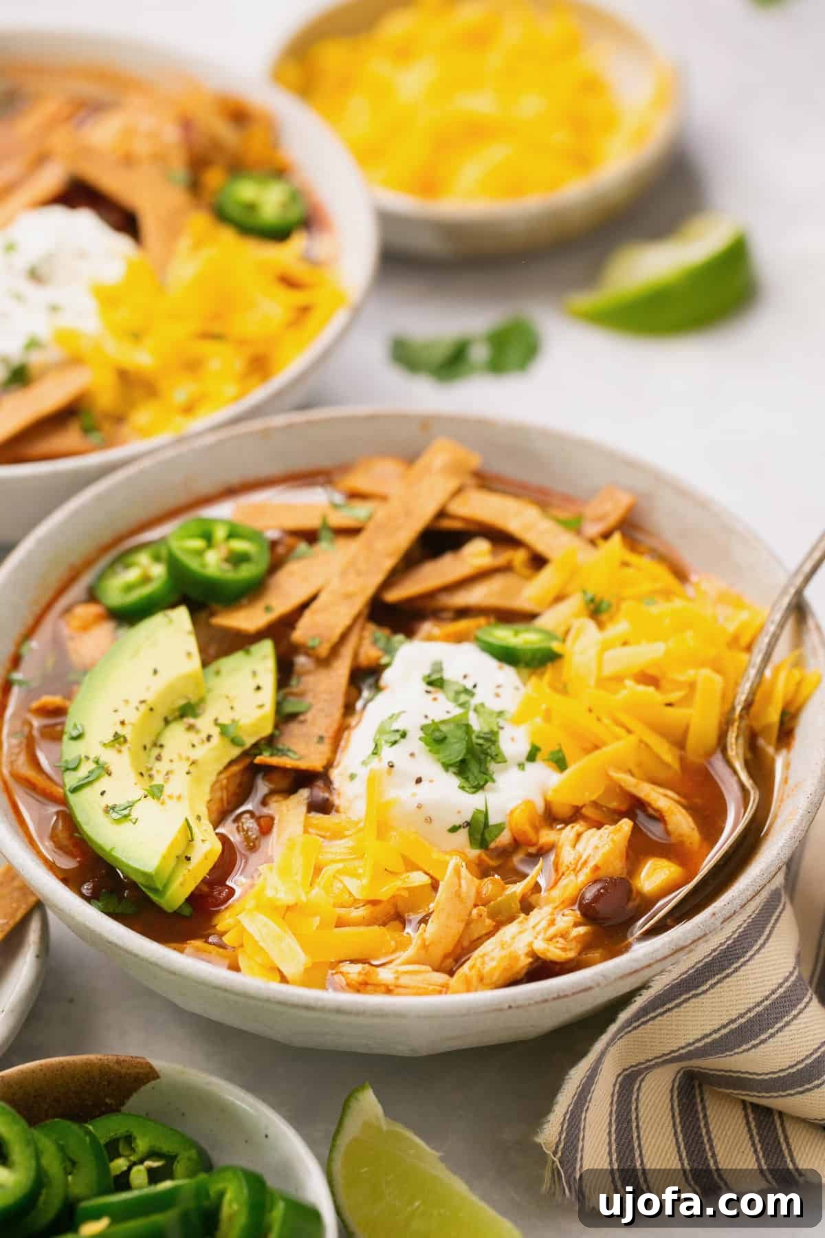 A closeup shot of tortilla soup in a white bowl topped with avocado, cheese, sour cream, and cilantro