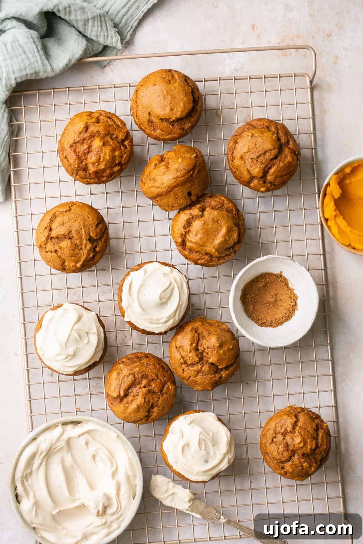 Moist Dairy-Free Pumpkin Muffins with Tangy Cream Cheese Frosting 6 An inviting overhead shot of delicious pumpkin muffins cooling on a baking rack, with some already adorned with a swirl of creamy frosting.