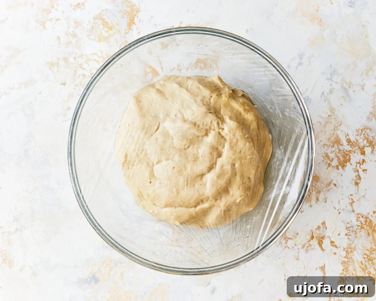 Irresistible Gluten-Free Cinnamon Buns 10 A ball of gluten-free dough in a greased glass bowl, covered with plastic wrap, resting for its first rise.
