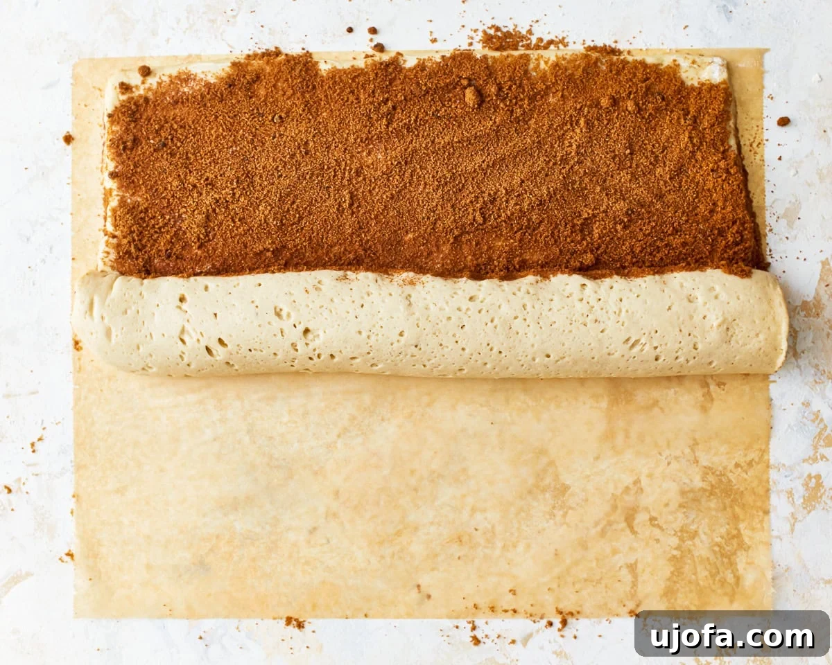 Irresistible Gluten-Free Cinnamon Buns 16 Hands carefully rolling up the gluten-free cinnamon roll dough from one end to form a log.