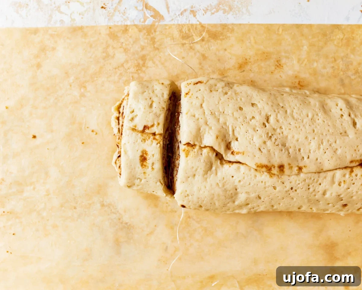 Irresistible Gluten-Free Cinnamon Buns 17 A log of gluten-free cinnamon roll dough being cut into individual rolls using dental floss for clean cuts.