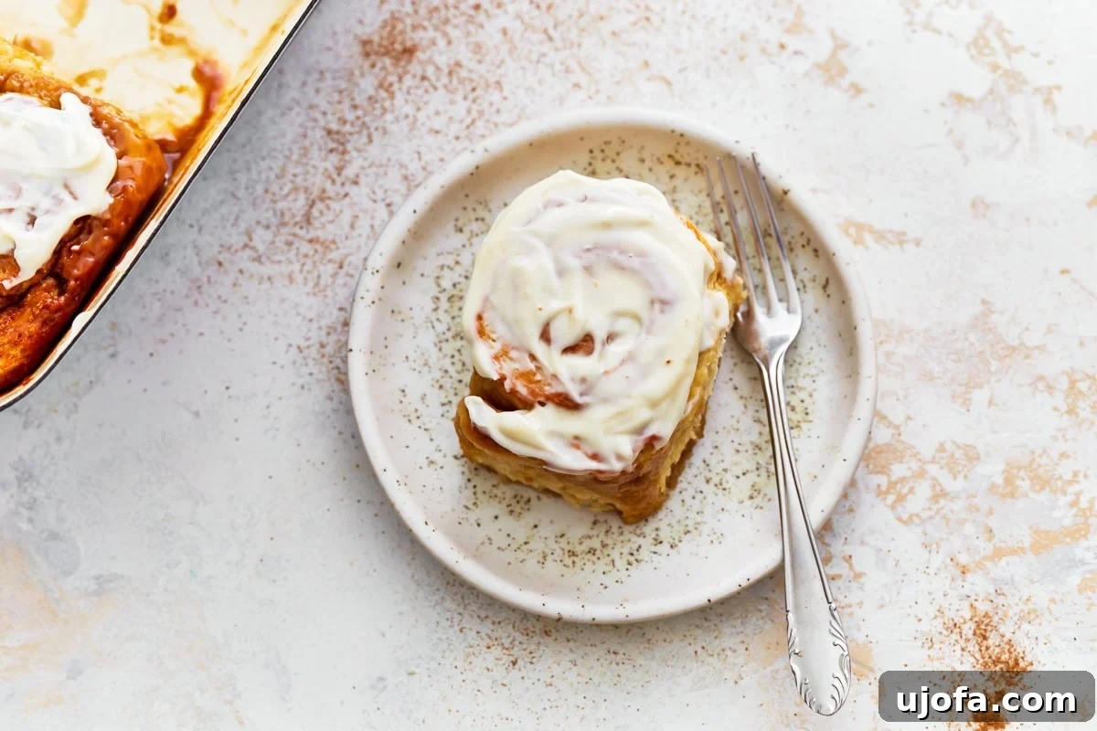 Irresistible Gluten-Free Cinnamon Buns 22 A single frosted gluten-free cinnamon roll, perfectly swirled, sitting on a speckled ceramic plate with a fork.