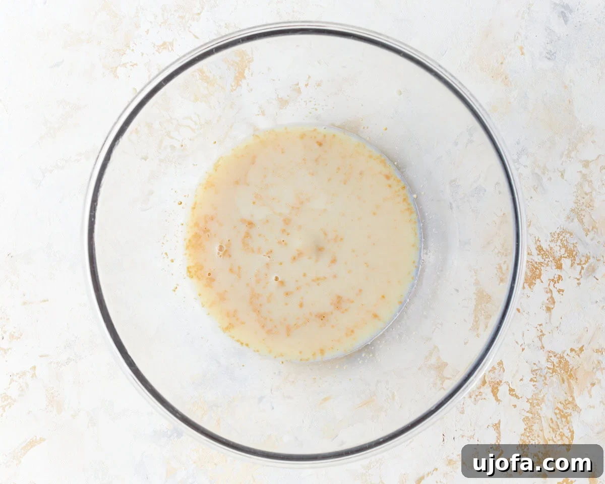 Irresistible Gluten-Free Cinnamon Buns 5 A glass bowl containing warm milk and granulated sugar, with yeast sprinkled on top, ready for proofing.