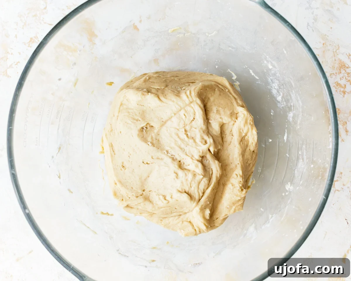 Irresistible Gluten-Free Cinnamon Buns 9 Kneaded gluten-free dough in a glass bowl, appearing soft and slightly tacky, ready for its first rise.