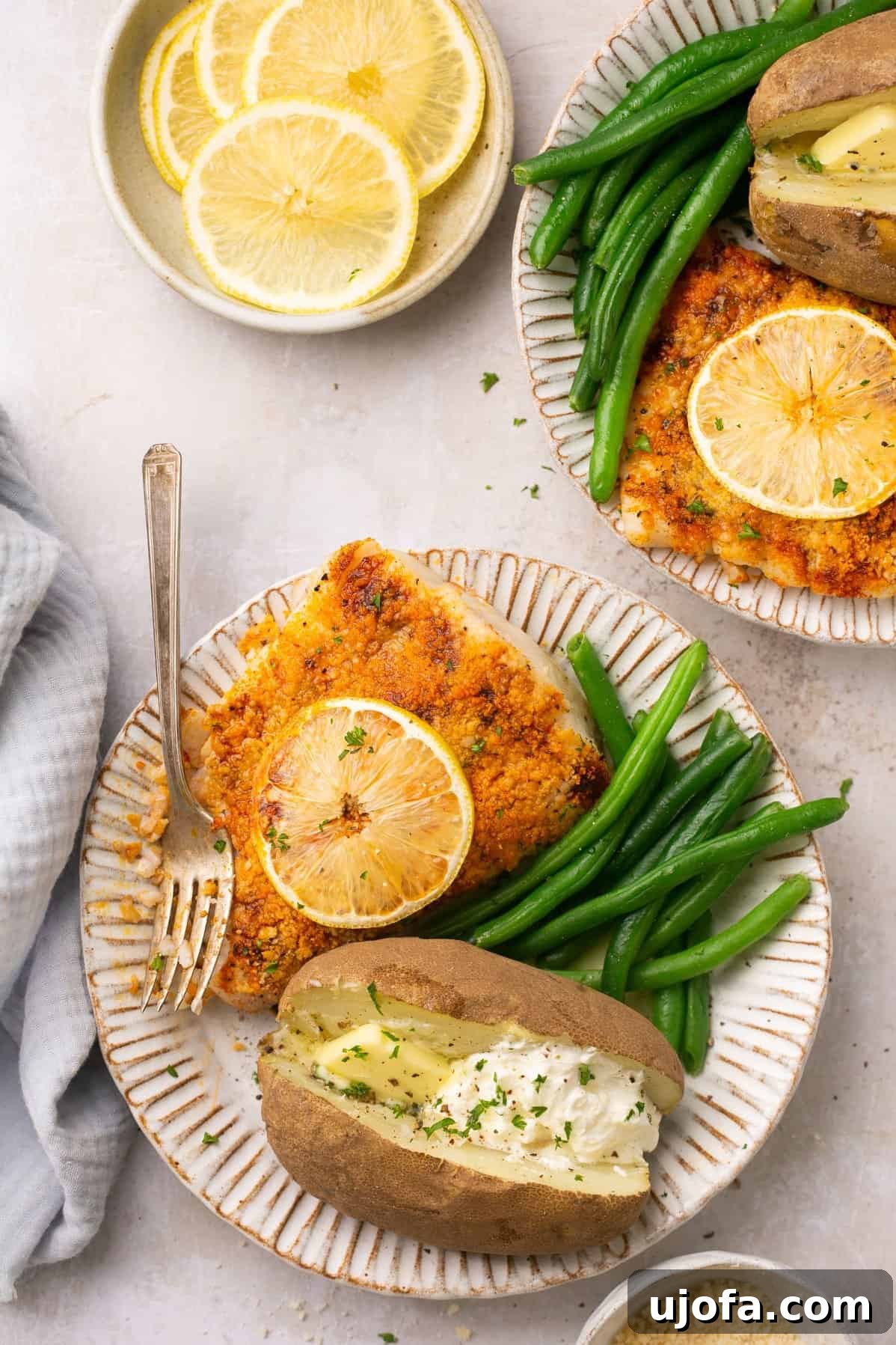 Two plates featuring beautifully air-fried halibut fillets topped with fresh lemon slices, served alongside vibrant green beans and a perfectly baked potato.