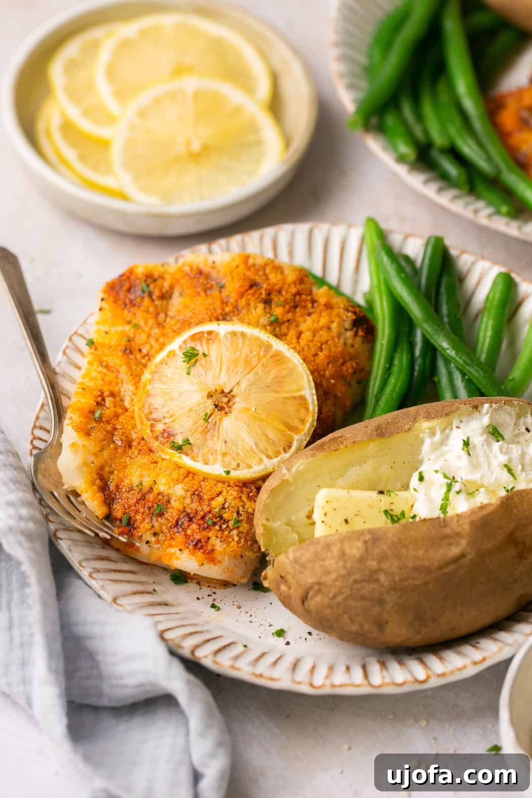 A close-up shot of a white plate featuring a generous serving of air-fried halibut, perfectly paired with vibrant green beans and a tender baked potato, ready to be enjoyed as a complete meal.