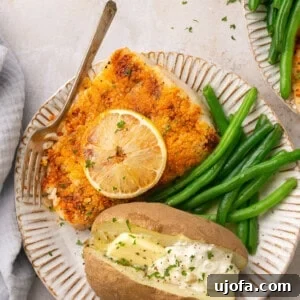 Air fryer halibut served on a white plate with a side of green beans and a baked potato topped with butter and sour cream, showcasing a complete and appetizing meal.