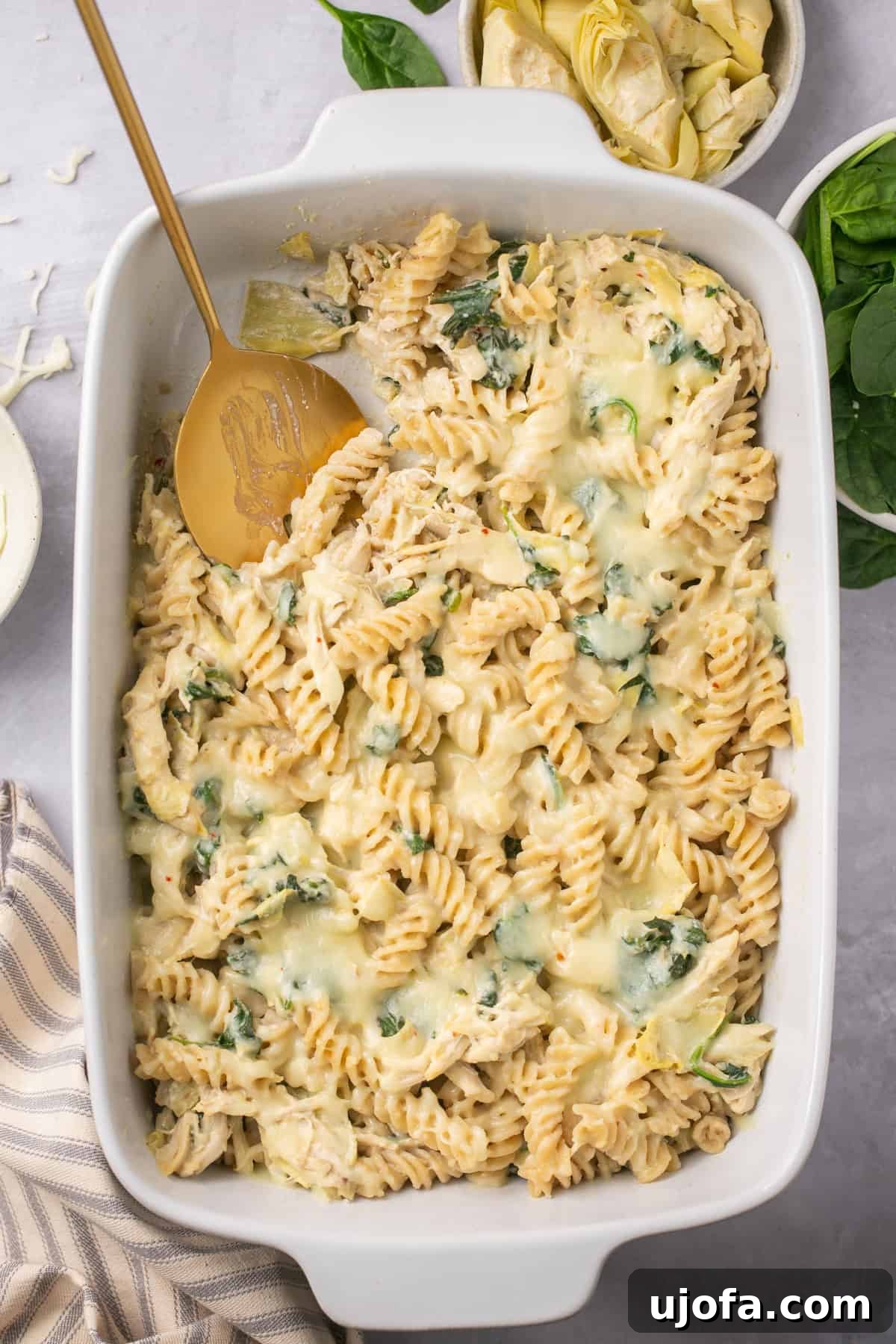 an overhead view of spinach artichoke chicken casserole in a white baking dish, ready to serve.
