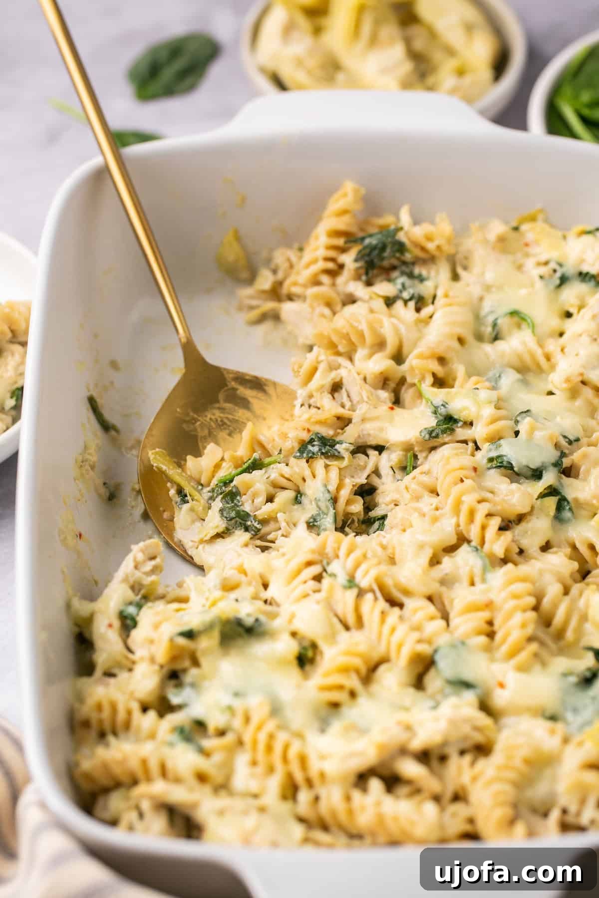 a gold serving spoon scooping out a serving of spinach artichoke chicken pasta, highlighting its creamy texture.