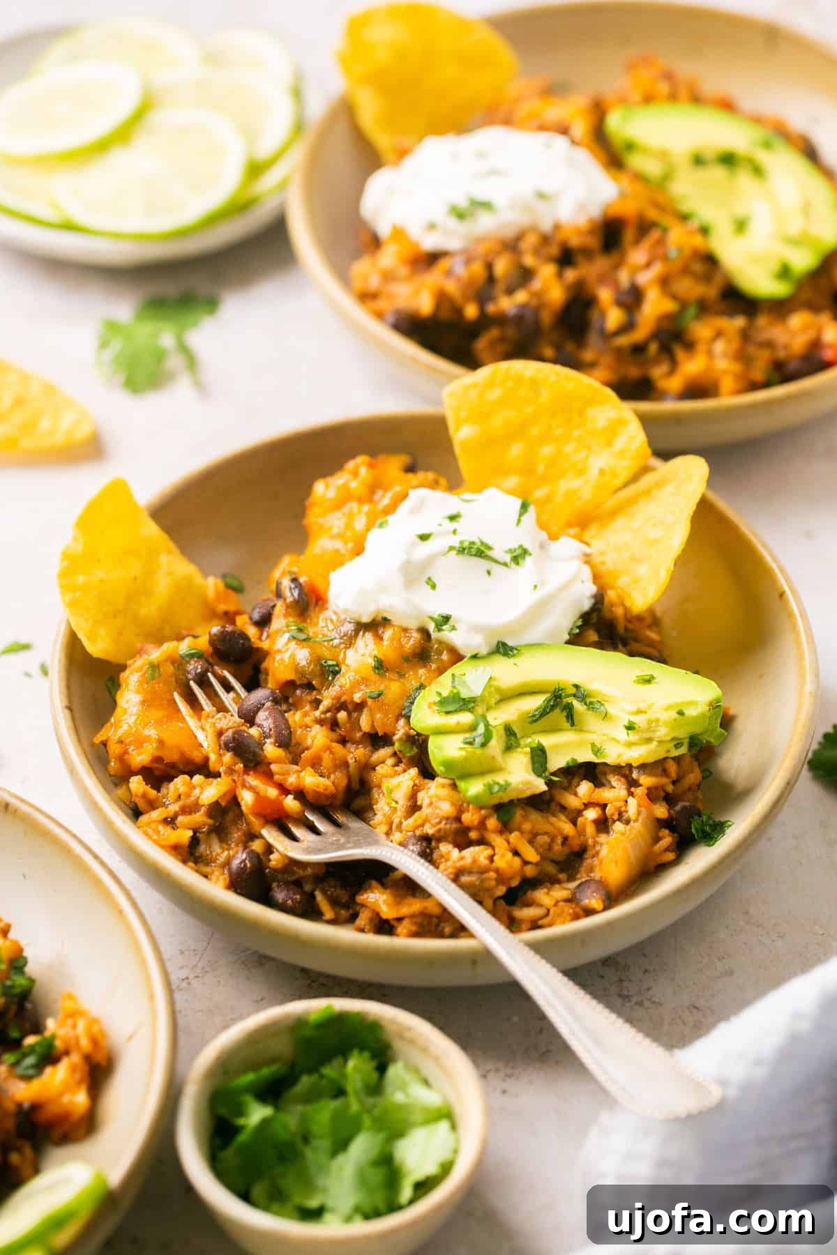A perfectly prepared bowl of taco in a bowl recipe fillings, artfully topped with creamy avocado slices, a dollop of sour cream, and fresh cilantro, with a silver fork invitingly placed beside it.