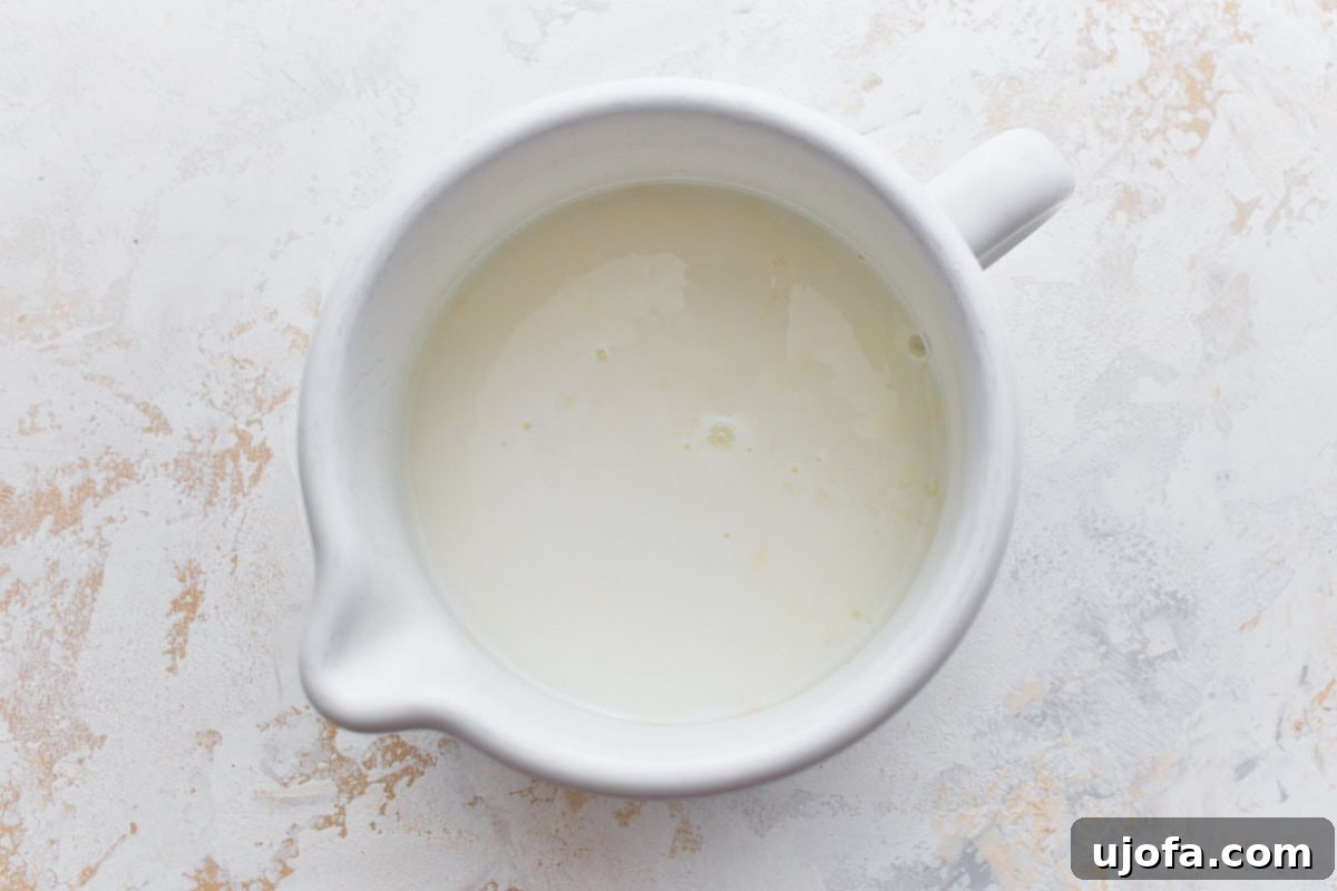 Deliciously Simple Gluten-Free Irish Soda Bread 5 A white ceramic bowl filled with liquid, possibly buttermilk or a milk mixture, on a light countertop