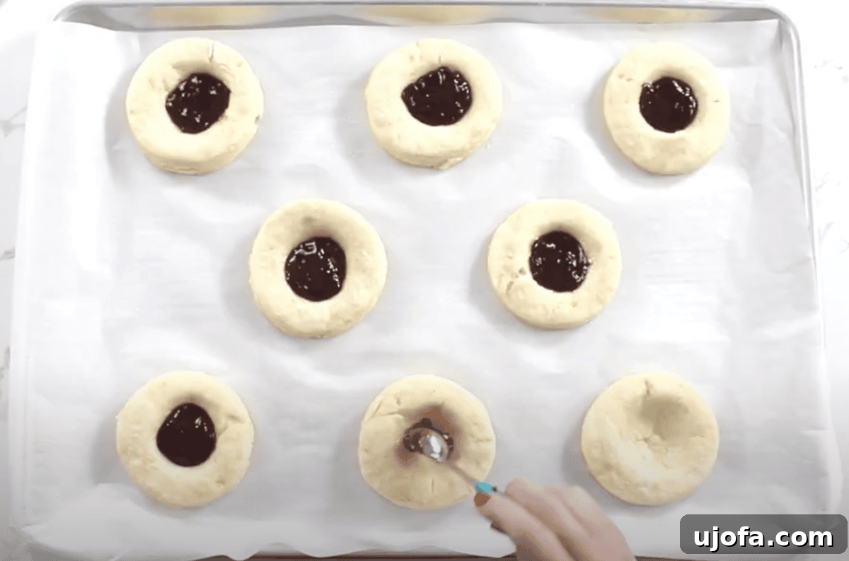 Each dough round has been filled with raspberry jam, with one more being filled using a small spoon.