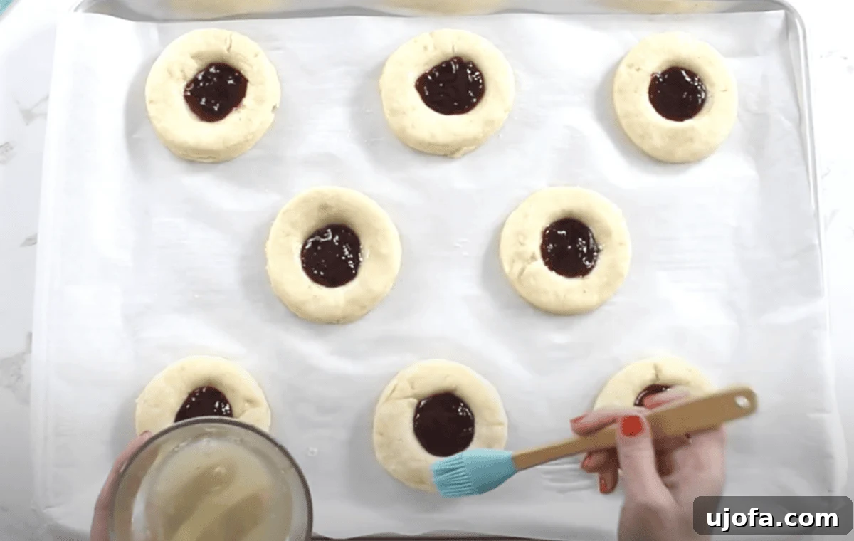 A pastry brush is used to apply an egg wash around the edges of the jam-filled Danish rounds before baking.
