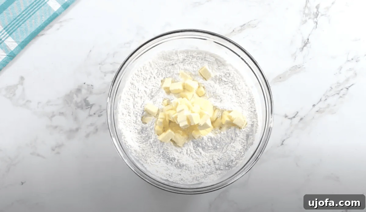 Cubes of softened butter are added to the flour mixture in a glass mixing bowl, ready to be cut in using a pastry cutter