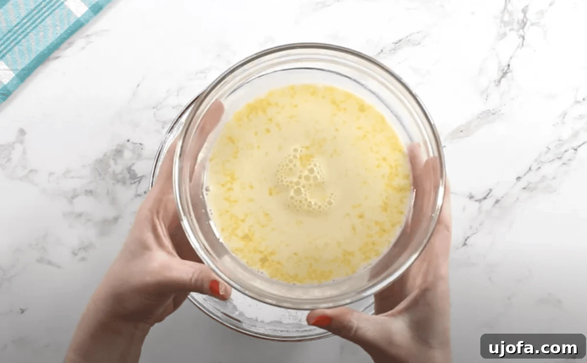 A glass bowl filled with a whisked mixture of milk, egg yolks, vanilla, almond extract, and salt, held over the flour mixture.