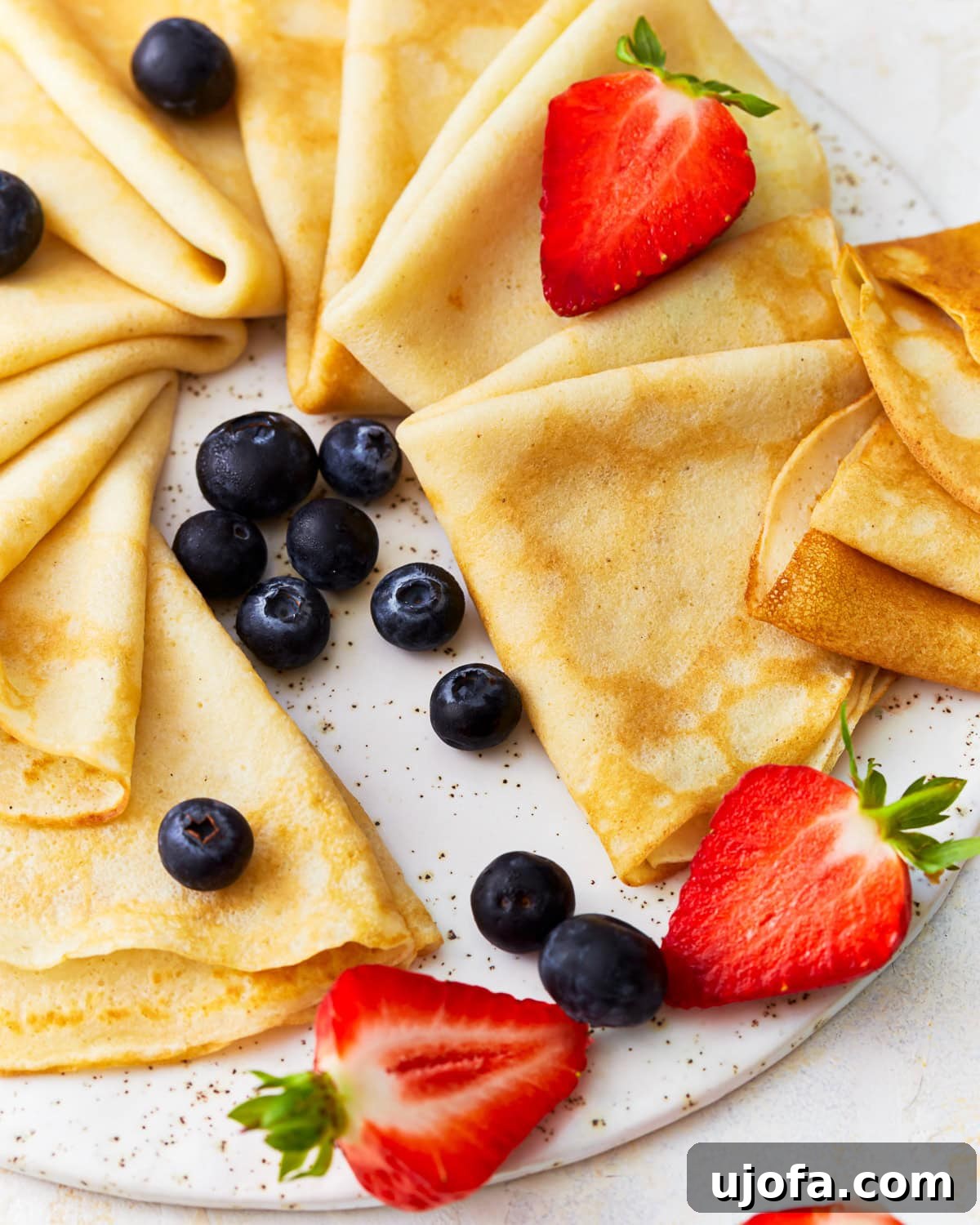 Gluten Free Brunch Delights 11 Delicate triangles of gluten-free crepes, artfully arranged on a large platter and adorned with a colorful assortment of fresh fruit, ready to be served.