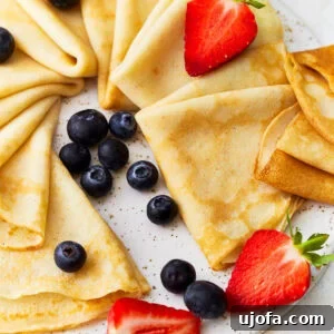 Gluten Free Brunch Delights 12 Delicate triangles of gluten-free crepes, artfully arranged on a large platter and adorned with a colorful assortment of fresh fruit, ready to be served.