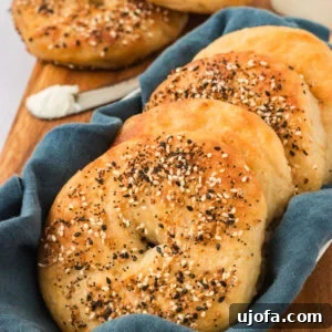 Gluten Free Brunch Delights 16 A collection of golden-brown gluten-free everything bagels, neatly arranged in a white basket lined with a blue cloth, presented on a wooden board alongside a creamy spread of cream cheese.