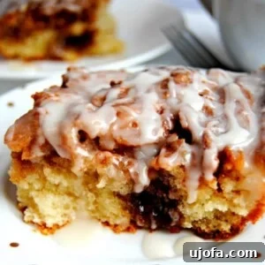 Gluten Free Brunch Delights 50 A single slice of moist gluten-free cinnamon roll cake on a white plate, with another slice and a coffee cup artfully blurred in the background.