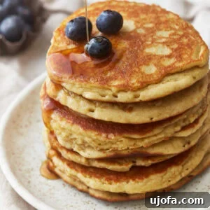 Gluten Free Brunch Delights 6 A three-quarters view of a tempting stack of almond flour pancakes on a white plate, adorned with fresh blueberries and a generous drizzle of maple syrup.