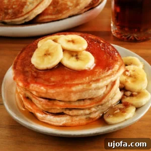 Gluten Free Brunch Delights 7 A delightful serving of gluten-free banana pancakes on a pristine white plate, with a larger stack of pancakes and a syrup pitcher artfully blurred in the background.