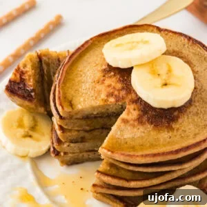 Gluten Free Brunch Delights 8 A close-up of a stack of fluffy banana oatmeal pancakes on a white plate, elegantly topped with fresh banana slices and generously drizzled with maple syrup. A piece has been cut out, revealing the soft interior.