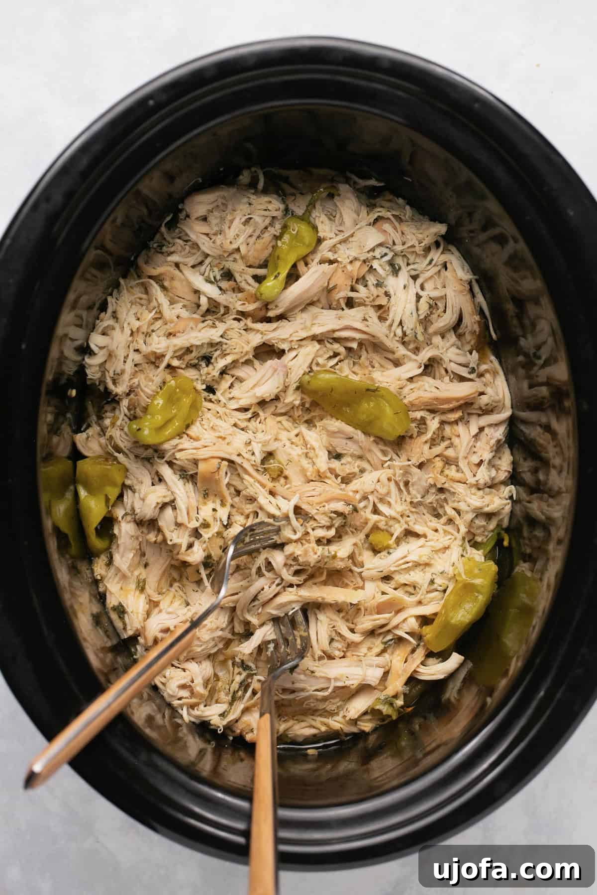 Mississippi Chicken Three Simple Variations 5 A slow cooker filled with bubbling, tender Mississippi chicken, generously garnished with whole pepperoncini peppers, ready to be shredded.