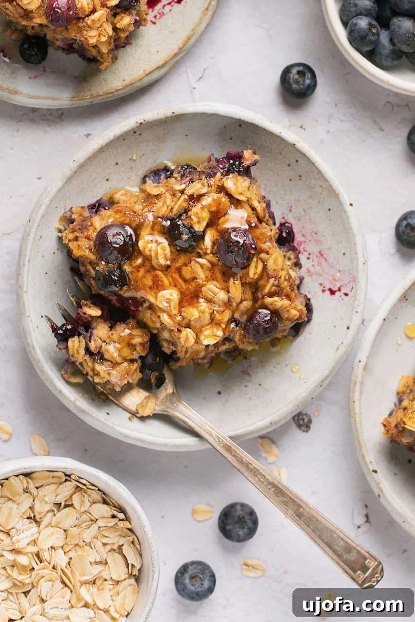 A close-up shot of a sliced portion of baked oatmeal, adorned with fresh blueberries and a drizzle of maple syrup