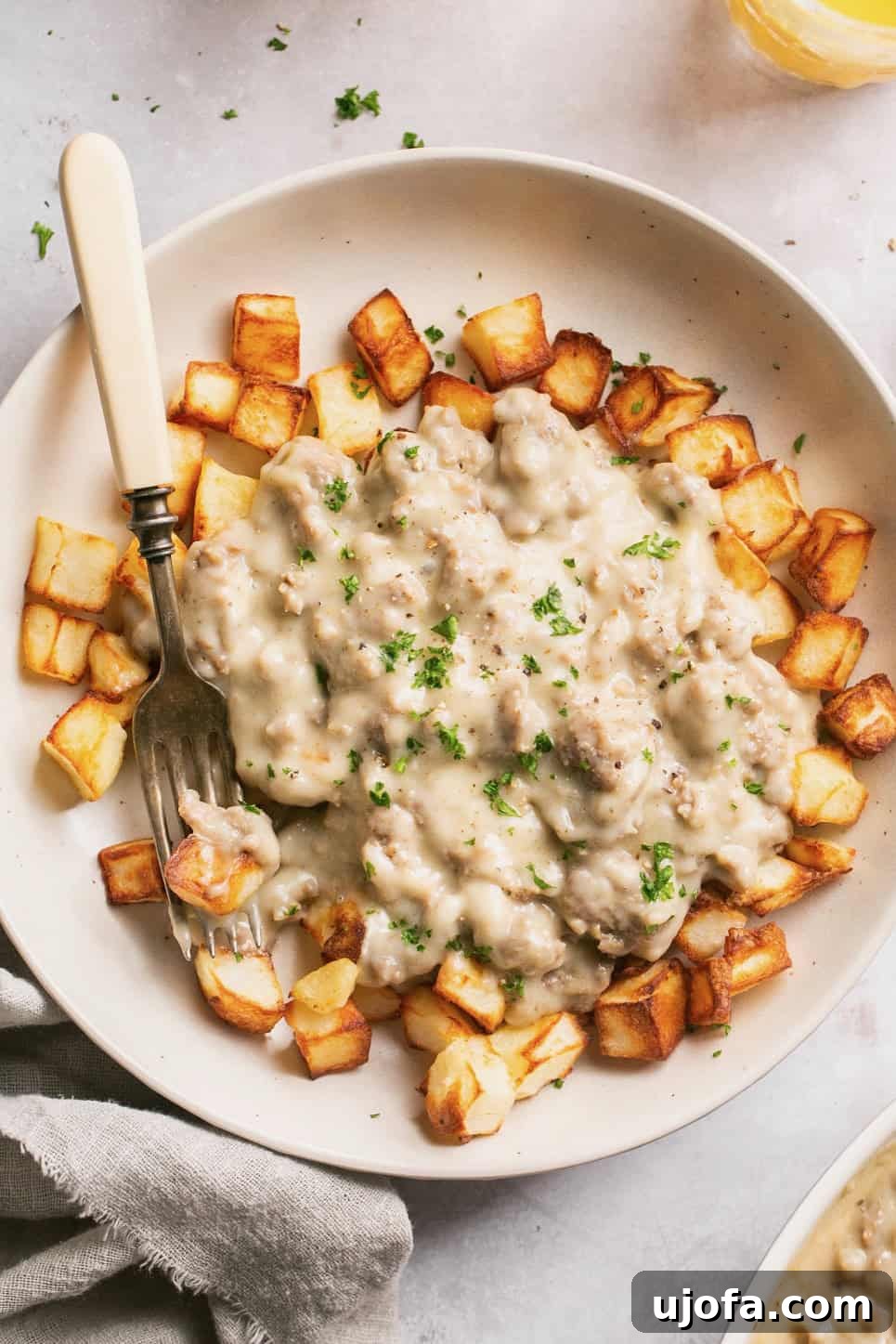 A closeup of rich, creamy keto sausage gravy generously poured over crispy air-fried potatoes, with a fork resting casually on the side.