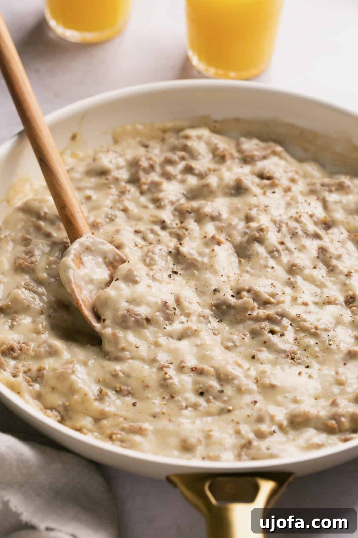 A wooden spoon gently stirring rich, creamy sausage gravy in a pristine white skillet, highlighting the smooth texture.