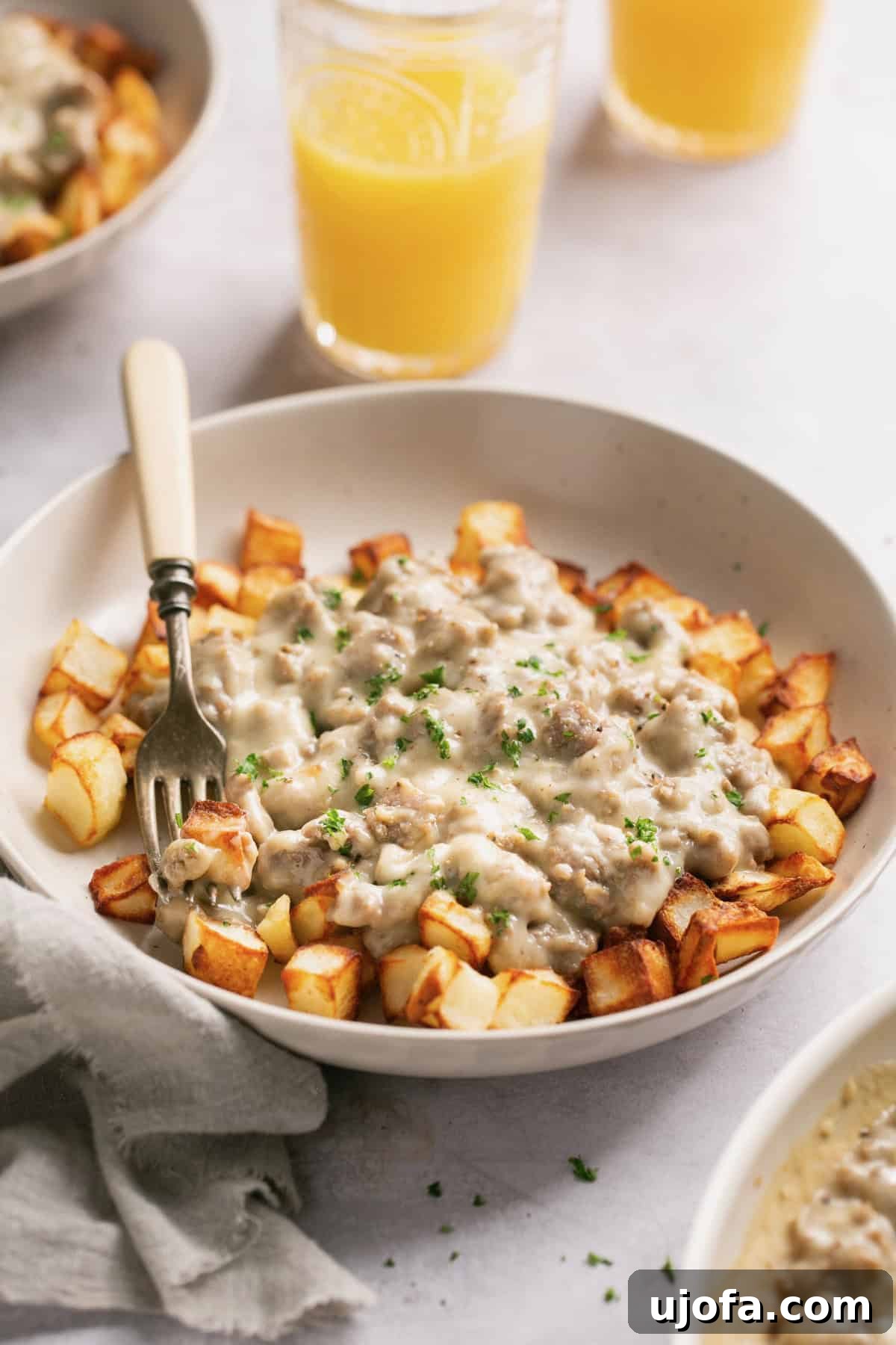 A bowl filled with crispy air-fried potatoes topped with creamy keto sausage gravy, with a fork poised for a bite.