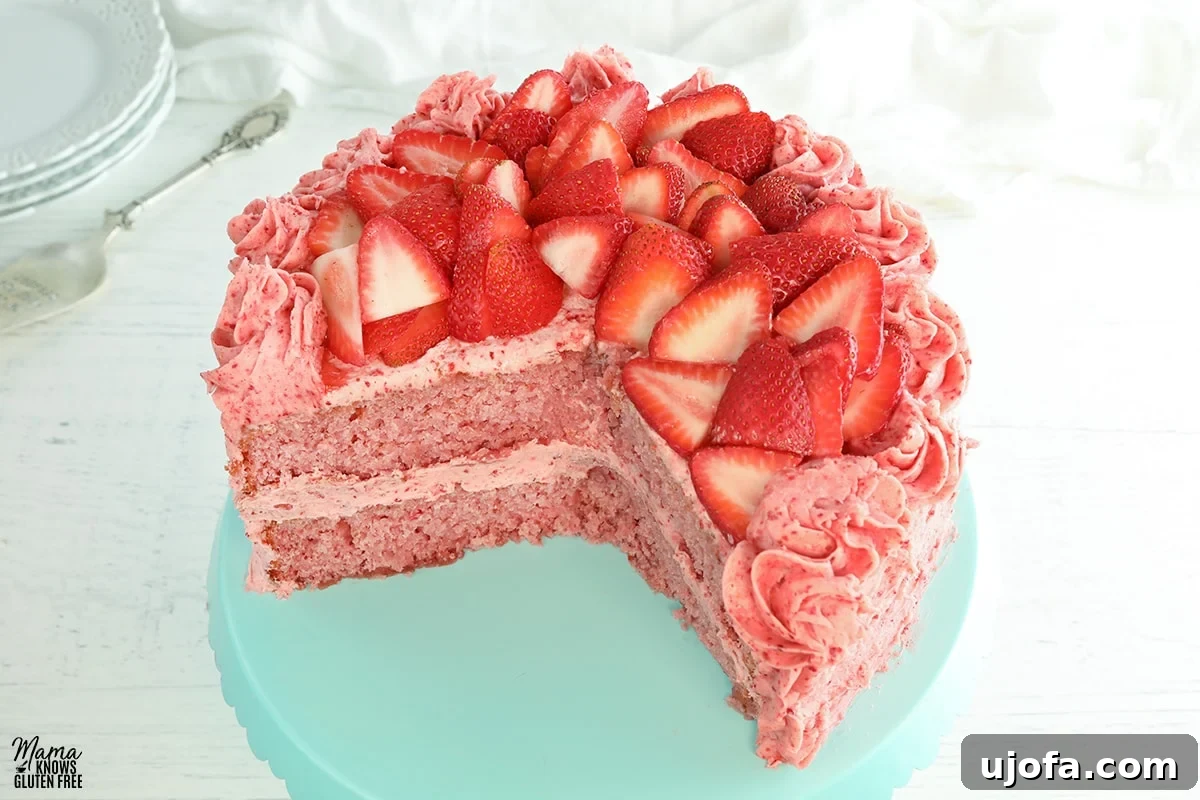 Luscious Strawberry Gluten-Free Cake 2 A perfectly sliced gluten-free strawberry cake on a elegant blue cake stand, showcasing its pink layers and creamy frosting, garnished with fresh strawberries.