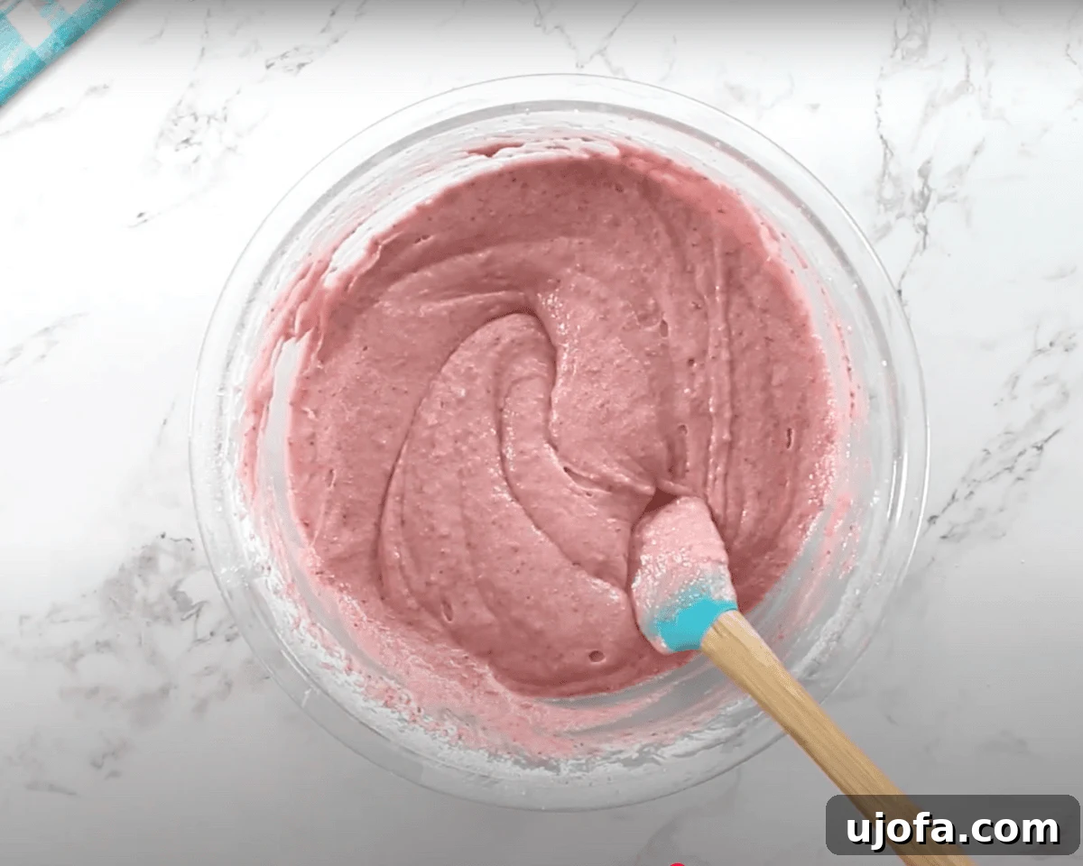Luscious Strawberry Gluten-Free Cake 13 A fully mixed gluten-free strawberry cake batter with a pinkish hue is being stirred with a silicone spatula.