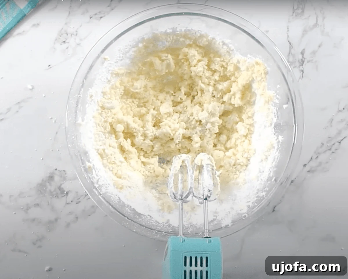 Luscious Strawberry Gluten-Free Cake 18 A glass mixing bowl with powdered sugar added to the whipped butter, forming a crumbly mixture before being fully blended.